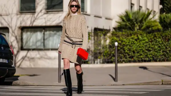 PARIS, FRANCE - FEBRUARY 06: Natalia Verza wears black sunglasses, a white tulle high neck from Givenchy, a beige braided wool pullover, a red shiny leather malle handbag from Moynat, black shiny leather belts, a silver chain belt, a crystal / rhinestones belt , black shiny leather wedge heels Shark knees boots from Givenchy , during a street style fashion photo session, on February 06, 2023 in Paris, France. (Photo by Edward Berthelot/Getty Images)