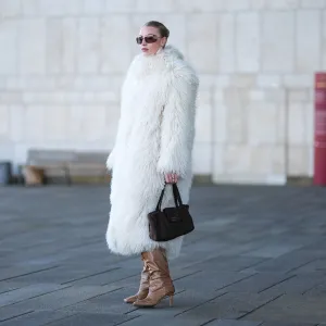 A guest wears Miu Miu sunglasses, a white oversized fluffy long faux fur coat , a Chanel bag, high heels pointed boots in brown leather, dark pink lipstick, outside OperaSport, during the Copenhagen Fashion Week AW24 on January 31, 2024 in Copenhagen, Denmark.