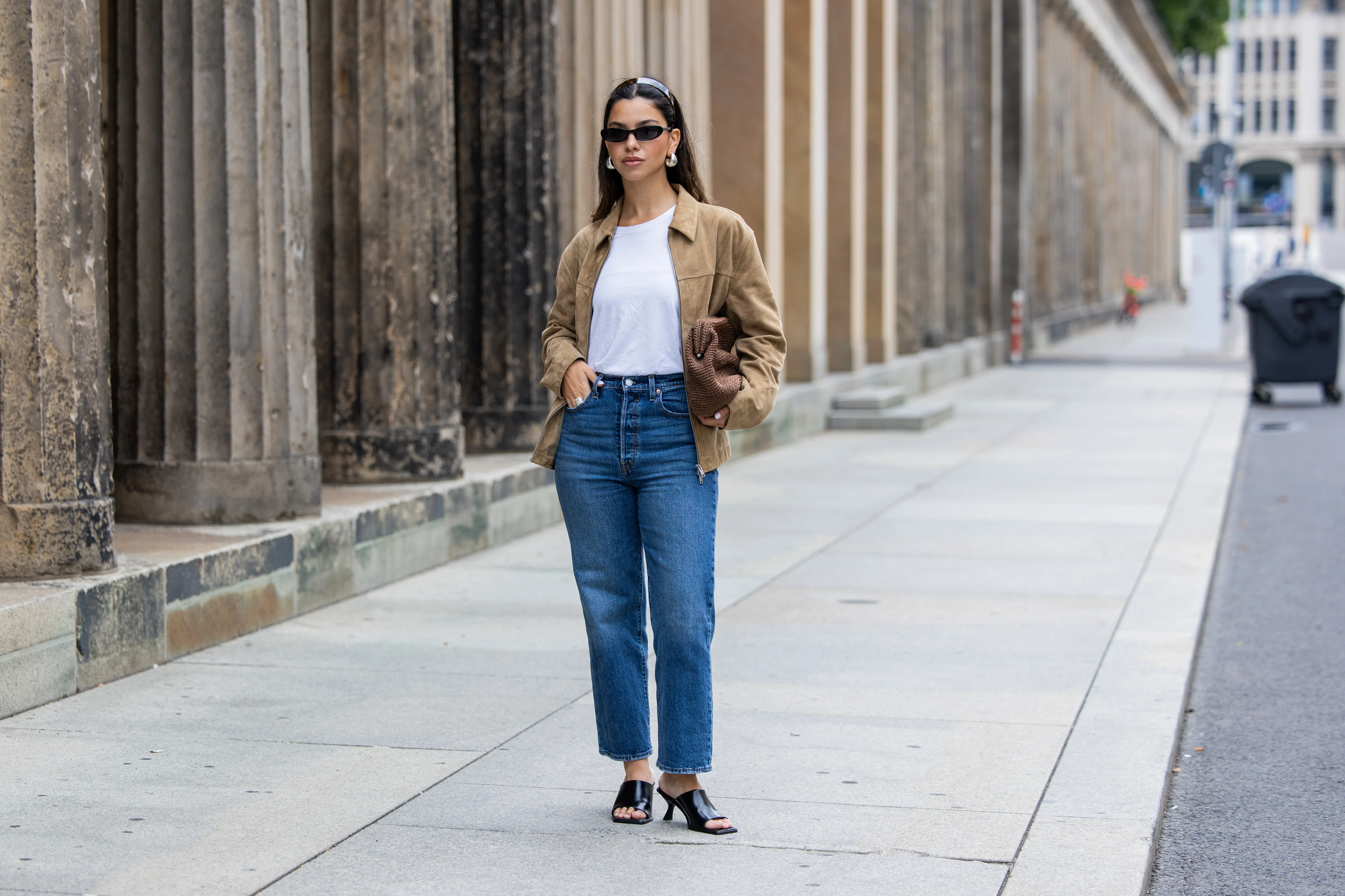 Bella Emar wears Levi’s blue denim jeans, white Cos t-shirt, brown Massimo Dutti Jacket, black H&M Heels, Mango sunglasses during the Berlin Fashion Week SS25 on July 01, 2024 in Berlin, Germany.