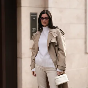 Leo Eberlin is seen wearing oval sunglasses with dark Havana frame and pink lenses and a gold logo at the temples from Miu Miu, a calf-length beige trench coat with double button placket and large notch lapels from Zara, a white cashmere turtleneck pullover with ribbed trims from Allude, beige jeans from Khaite, a diamond ring from Leo Mathild, and a rectangular small white leather bag from Loro Piana on October 03, 2024 in Berlin, Germany.
