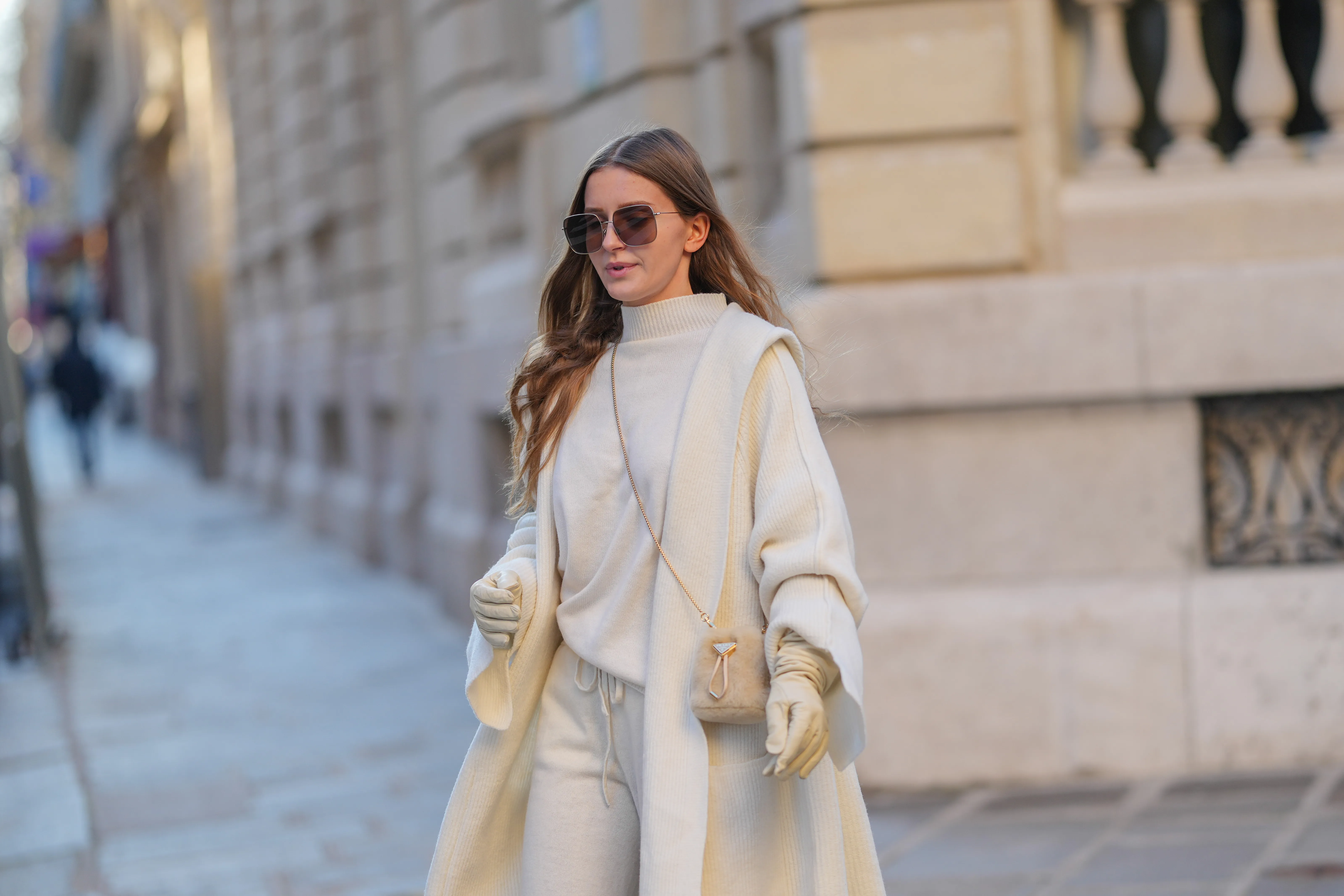 Diane Batoukina wears brown Dior sunglasses, a white cashmere Zara turtleneck pullover, matching coat and pants, a light brown fluffy faux fur Prada bag, white leather gloves, during a street style fashion photo session, on January 13, 2025 in Paris, France.