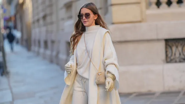 Diane Batoukina wears brown Dior sunglasses, a white cashmere Zara turtleneck pullover, matching coat and pants, a light brown fluffy faux fur Prada bag, white leather gloves, during a street style fashion photo session, on January 13, 2025 in Paris, France.