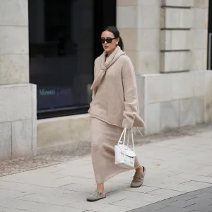 Laura Noltemeyer is seen wearing an oversized beige alpaca wool sweater with tie-back detailing by Aylin König; a long alpaca wool knit skirt in a straight cut by Aylin König; an alpaca knit scarf draped and knotted around the neck by Aylin König; beige suede Boston clogs by Birkenstock; a white intrecciato leather handbag called „Arco Bag“ by Bottega Veneta; slim black cat-eye sunglasses by Yves Saint Laurent; gold statement earrings with a green stone detail by Mango; her brown and straight hair is tied in a low ponytail on October 16, 2025 in Hamburg, Germany.