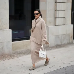Laura Noltemeyer is seen wearing an oversized beige alpaca wool sweater with tie-back detailing by Aylin König; a long alpaca wool knit skirt in a straight cut by Aylin König; an alpaca knit scarf draped and knotted around the neck by Aylin König; beige suede Boston clogs by Birkenstock; a white intrecciato leather handbag called „Arco Bag“ by Bottega Veneta; slim black cat-eye sunglasses by Yves Saint Laurent; gold statement earrings with a green stone detail by Mango; her brown and straight hair is tied in a low ponytail on October 16, 2025 in Hamburg, Germany.