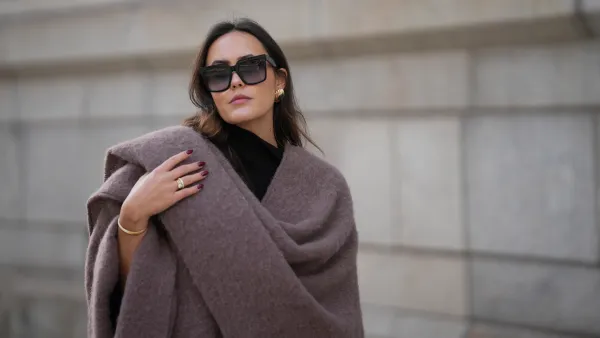 Laura Noltemeyer is seen wearing an oversized fringed wool poncho in a mauve tone with a textured, fluffy finish, fringes at the hem and a gold pin closure element called „Poncho COZY“ by Aylin Koenig; black fine-knit turtleneck sweater with slim-fitting silhouette by Aylin Koenig; among her jewelry is a white gold „LOVE“ bracelet by Cartier; oversized square black acetate sunglasses with ombré tinted lenses by Céline; large gold statement earrings with a ruffled surface and a green stone element by Mango; her dark brown hair is styled in loose waves with a center part on November 13, 2025 in Hamburg, Germany.