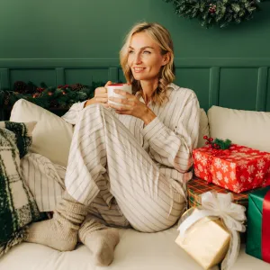 A beautiful blonde woman is sitting on the sofa in the Christmas living room and drinking coffee.