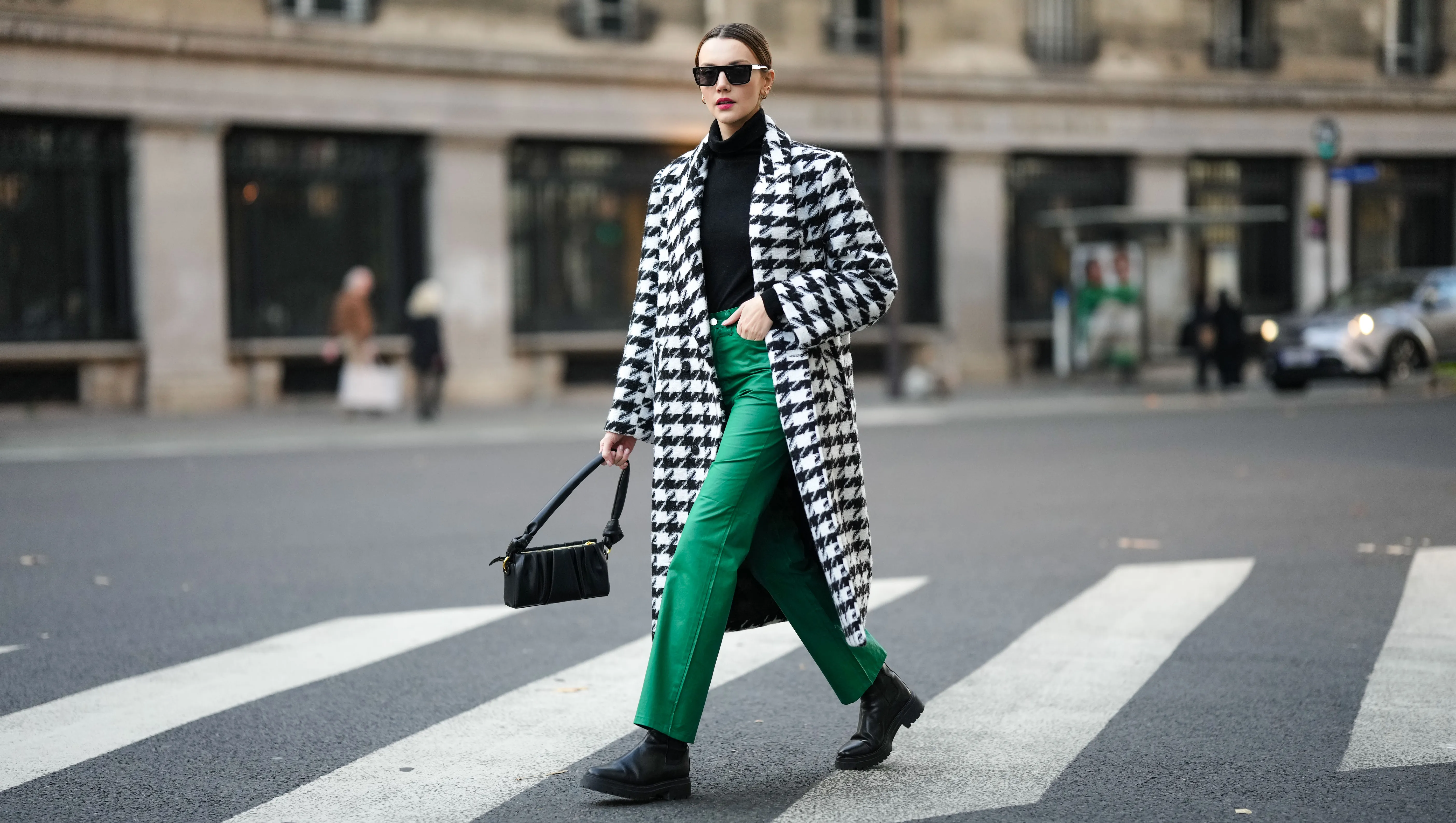 PARIS, FRANCE - NOVEMBER 11: Olesya Senchenko wears black sunglasses, gold earrings, a black wool turtleneck pullover, a black and white large houndstooths print pattern long coat, green denim large pants, gold rings, black shiny leather ankle boots, a black leather puffy shoulder bag, during a street style fashion photo session, on November 11, 2021 in Paris, France. (Photo by Edward Berthelot/Getty Images)