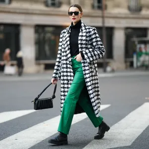 PARIS, FRANCE - NOVEMBER 11: Olesya Senchenko wears black sunglasses, gold earrings, a black wool turtleneck pullover, a black and white large houndstooths print pattern long coat, green denim large pants, gold rings, black shiny leather ankle boots, a black leather puffy shoulder bag, during a street style fashion photo session, on November 11, 2021 in Paris, France. (Photo by Edward Berthelot/Getty Images)