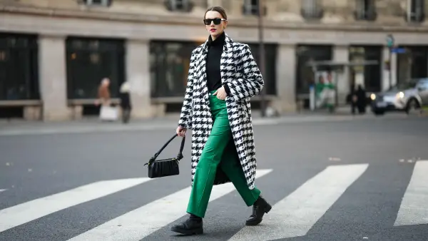 PARIS, FRANCE - NOVEMBER 11: Olesya Senchenko wears black sunglasses, gold earrings, a black wool turtleneck pullover, a black and white large houndstooths print pattern long coat, green denim large pants, gold rings, black shiny leather ankle boots, a black leather puffy shoulder bag, during a street style fashion photo session, on November 11, 2021 in Paris, France. (Photo by Edward Berthelot/Getty Images)