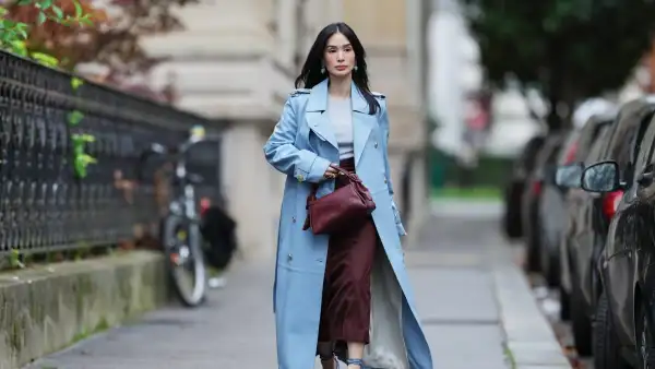 PARIS, FRANCE - NOVEMBER 07: Heart Evangelista wears long wavy black hair, a light blue leather double-breasted trench coat over a light gray knit top, burgundy wide-leg cropped trousers, blue feather-trimmed heeled sandals with ankle straps, a burgundy leather pouch bag, and turquoise drop earrings, during a street style fashion photo session, on November 07, 2025 in Paris, France. (Photo by Edward Berthelot/Getty Images)