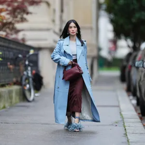 PARIS, FRANCE - NOVEMBER 07: Heart Evangelista wears long wavy black hair, a light blue leather double-breasted trench coat over a light gray knit top, burgundy wide-leg cropped trousers, blue feather-trimmed heeled sandals with ankle straps, a burgundy leather pouch bag, and turquoise drop earrings, during a street style fashion photo session, on November 07, 2025 in Paris, France. (Photo by Edward Berthelot/Getty Images)