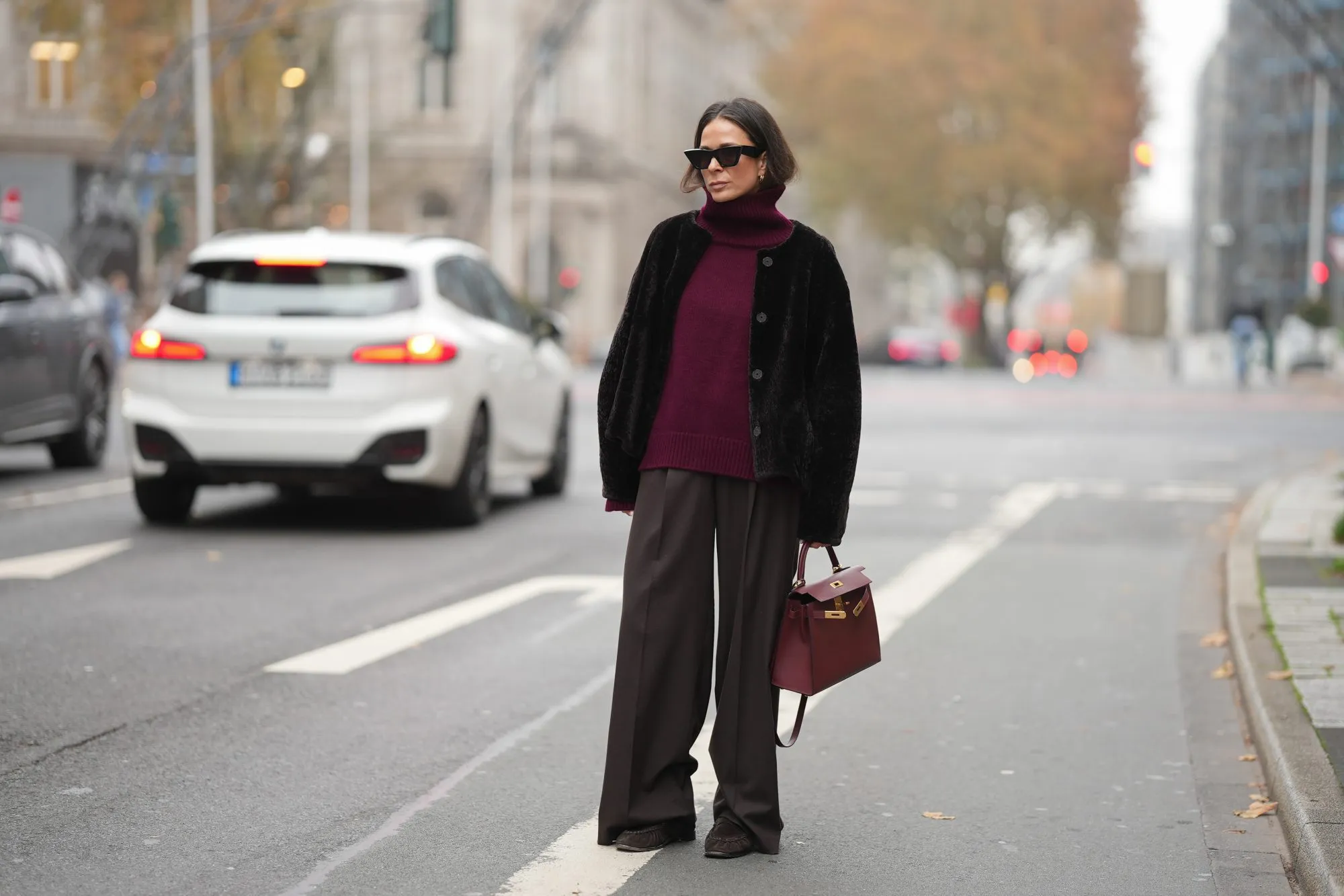 DUESSELDORF, GERMANY - NOVEMBER 10: Patricia Wirschke is seen wearing a dark brown shearling jacket with a boxy cut by Manzoni 24; a burgundy cashmere turtleneck sweater by Van Kukil; wide-leg tailored trousers in dark brown wool by Seductive; brown suede loafers with ruffled stitching by Yves Saint Laurent; a structured burgundy leather “Kelly 25” handbag with gold hardware in Rouge H by Hermès; black cat-eye sunglasses by Phoebe Philo; her brown hair is straight with a center parting and tucked into the collar on November 10, 2025 in Duesseldorf, Germany. (Photo by Moritz Scholz/Getty Images)