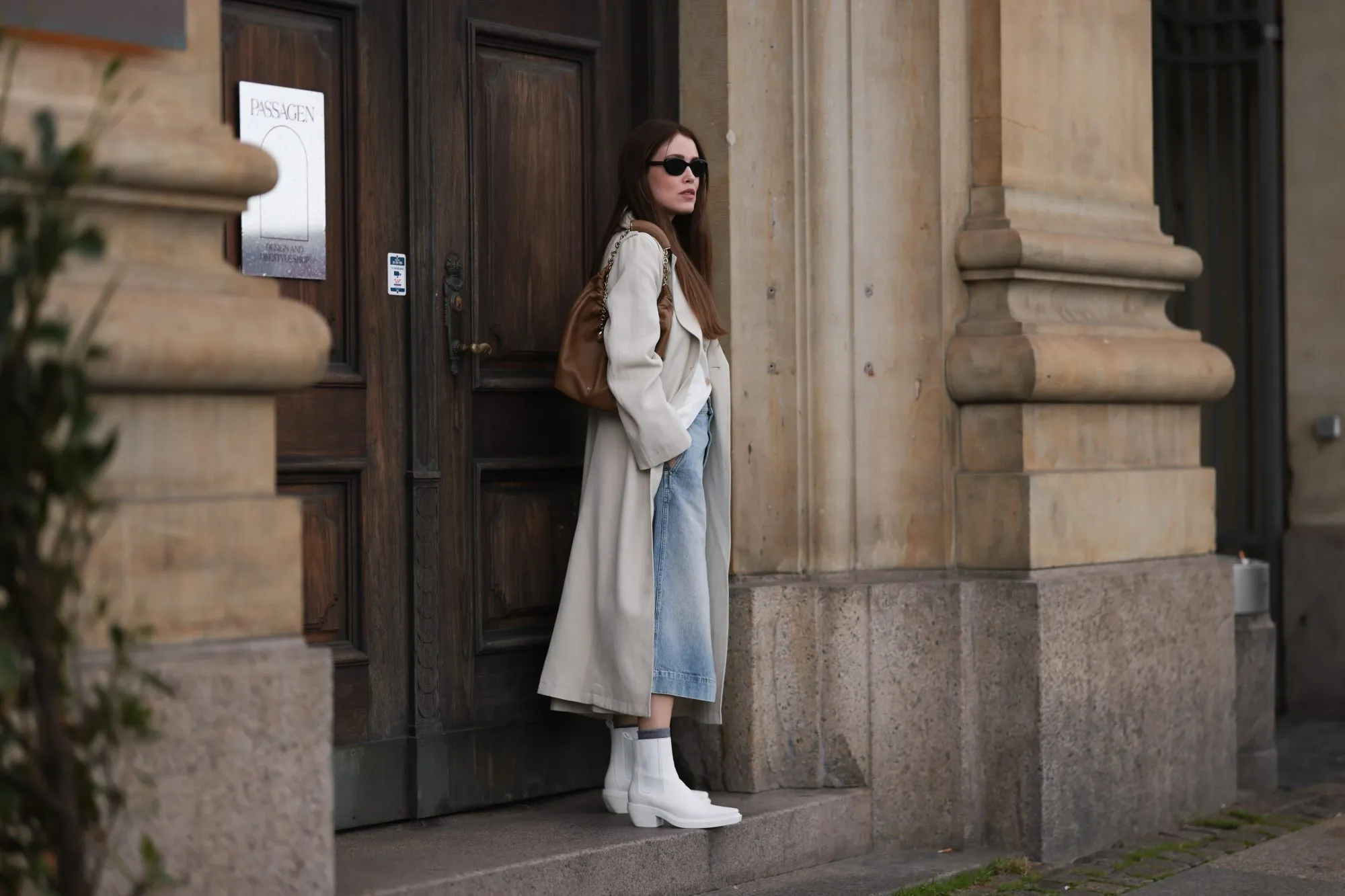 COPENHAGEN, DENMARK - AUGUST 10: Annabel Rosendahl seen wearing black sunglasses, white shirt, beige long coat, light blue denim skirt, brown leather bag and Copenhagen StudiosCPH236 Nappa White leather boots, on August 10, 2023 in Copenhagen, Denmark. (Photo by Jeremy Moeller/Getty Images for The Wants Social / Copenhagen Studios)