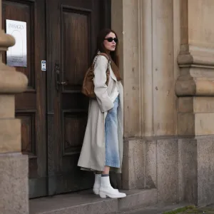 COPENHAGEN, DENMARK - AUGUST 10: Annabel Rosendahl seen wearing black sunglasses, white shirt, beige long coat, light blue denim skirt, brown leather bag and Copenhagen StudiosCPH236 Nappa White leather boots, on August 10, 2023 in Copenhagen, Denmark. (Photo by Jeremy Moeller/Getty Images for The Wants Social / Copenhagen Studios)