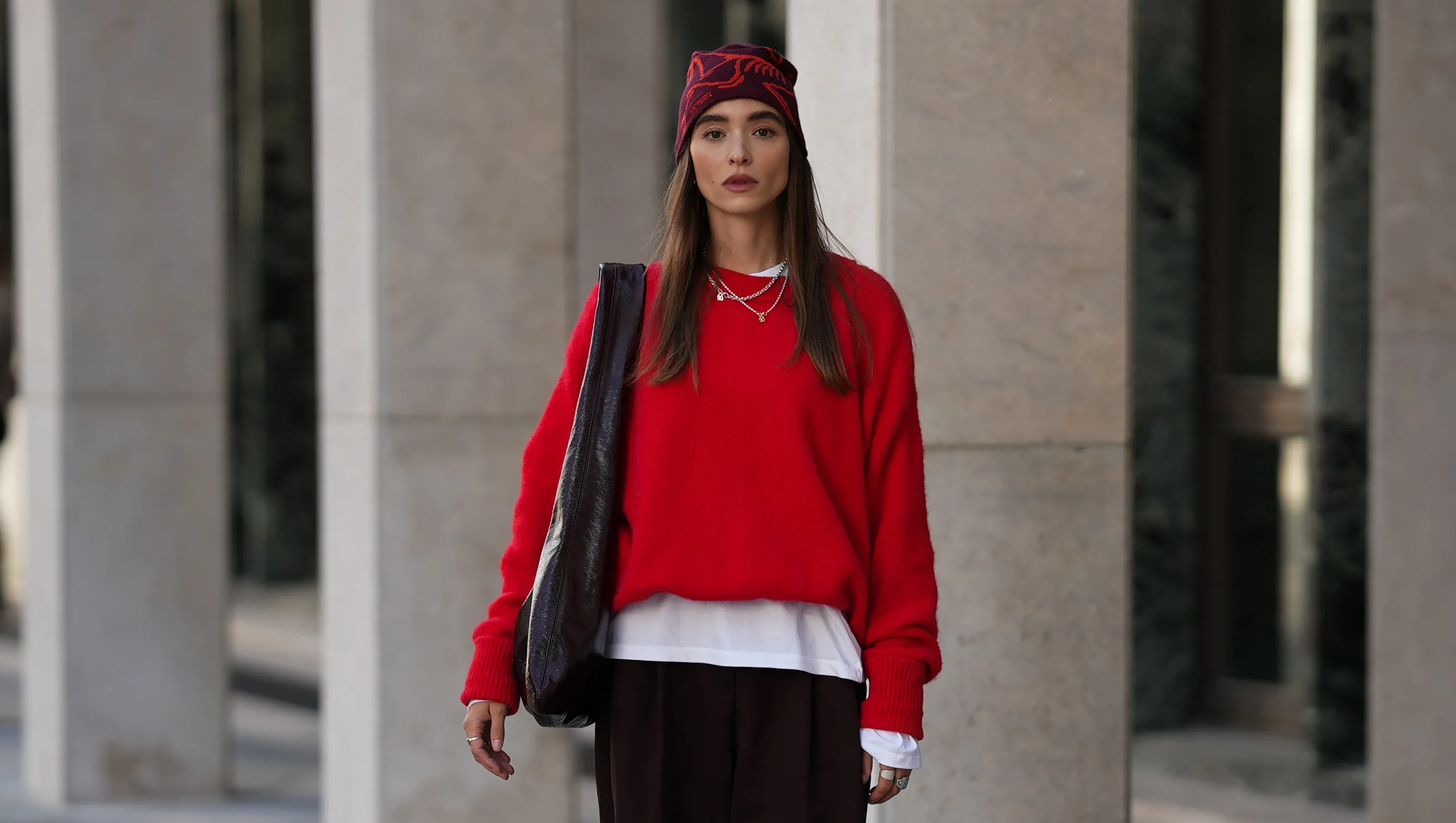 COLOGNE, GERMANY - SEPTEMBER 18: Evi Wave is seen wearing a bright red knit sweater with long sleeves from American Vintage; a white long-sleeved t-shirt, worn under the sweater from Weekday; wide-leg, brown trousers with a voluminous silhouette from COS; brown leather loafers with a subtle shine from Vagabond; a large bordeaux leather shoulder bag with a glossy shade from Arket; subtle silver jewellry, featuring metallic necklaces and rings from Ariane Ernst; a red patterned beanie from ArcTeryx; her brown hair is worn loose on September 18, 2025 in Cologne, Germany. (Photo by Moritz Scholz/Getty Images)