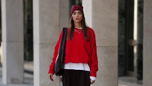 COLOGNE, GERMANY - SEPTEMBER 18: Evi Wave is seen wearing a bright red knit sweater with long sleeves from American Vintage; a white long-sleeved t-shirt, worn under the sweater from Weekday; wide-leg, brown trousers with a voluminous silhouette from COS; brown leather loafers with a subtle shine from Vagabond; a large bordeaux leather shoulder bag with a glossy shade from Arket; subtle silver jewellry, featuring metallic necklaces and rings from Ariane Ernst; a red patterned beanie from ArcTeryx; her brown hair is worn loose on September 18, 2025 in Cologne, Germany. (Photo by Moritz Scholz/Getty Images)