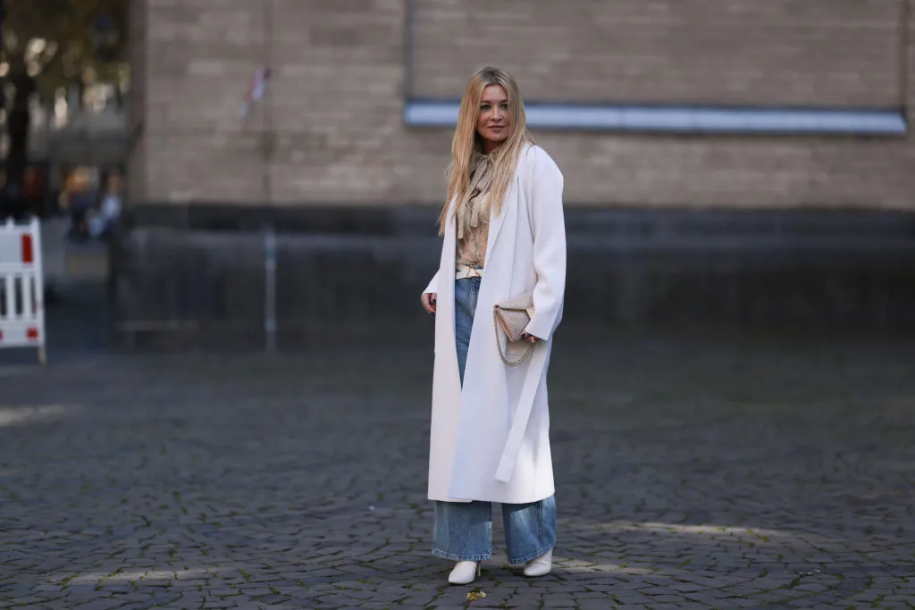 COLOGNE, GERMANY - OCTOBER 08: Tanja Comba is seen wearing beige/gold lace blouse from Valentino, blue denim pants from Khaite, creme white long knit cardigan/coat from Roberto Collina, beige glitter Valentino bag, white leather Bottega Veneta belt and white boots from Zara, on October 08, 2022 in Cologne, Germany. (Photo by Jeremy Moeller/Getty Images)