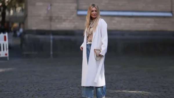 COLOGNE, GERMANY - OCTOBER 08: Tanja Comba is seen wearing beige/gold lace blouse from Valentino, blue denim pants from Khaite, creme white long knit cardigan/coat from Roberto Collina, beige glitter Valentino bag, white leather Bottega Veneta belt and white boots from Zara, on October 08, 2022 in Cologne, Germany. (Photo by Jeremy Moeller/Getty Images)