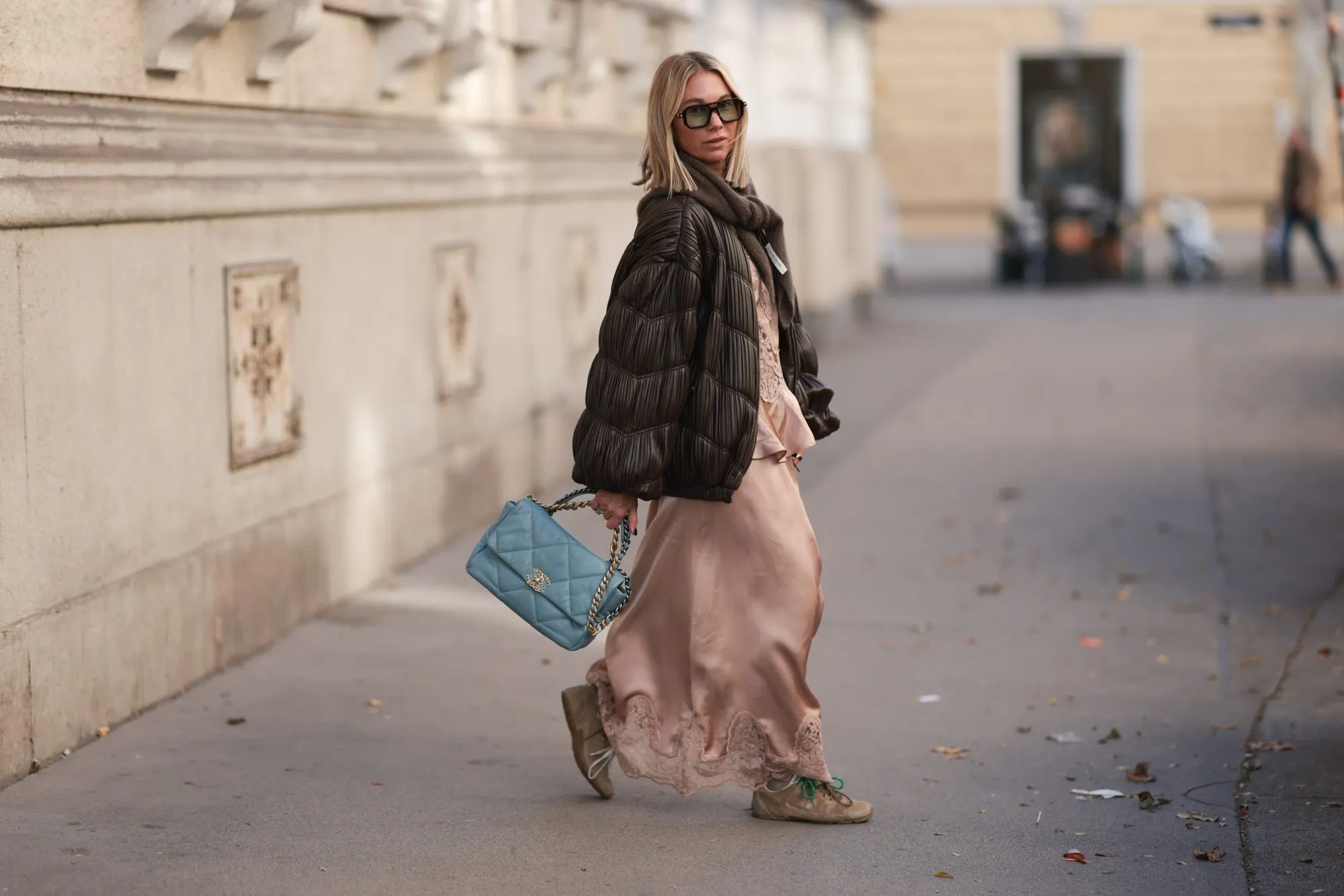 VIENNA, AUSTRIA - OCTOBER 20: Karin Teigl with blonde short and straight hair seen wearing a rose-colored H&M silk dress paired with a matching H&M silk top for a tonal layered look. She styles the outfit with a babyblue leather Chanel handbag, Rotate brown puffer jacket and Miu Miu x New Balance beige sneakers for a modern blend of elegance and casual comfort. Completing the ensemble, she adds a by Aylin Koenig brown cashmere scarf and Kuboraum brown sunglasses, creating a refined yet effortless street-style appearance on October 20, 2025 in Vienna, Austria. (Photo by Jeremy Moeller/Getty Images)