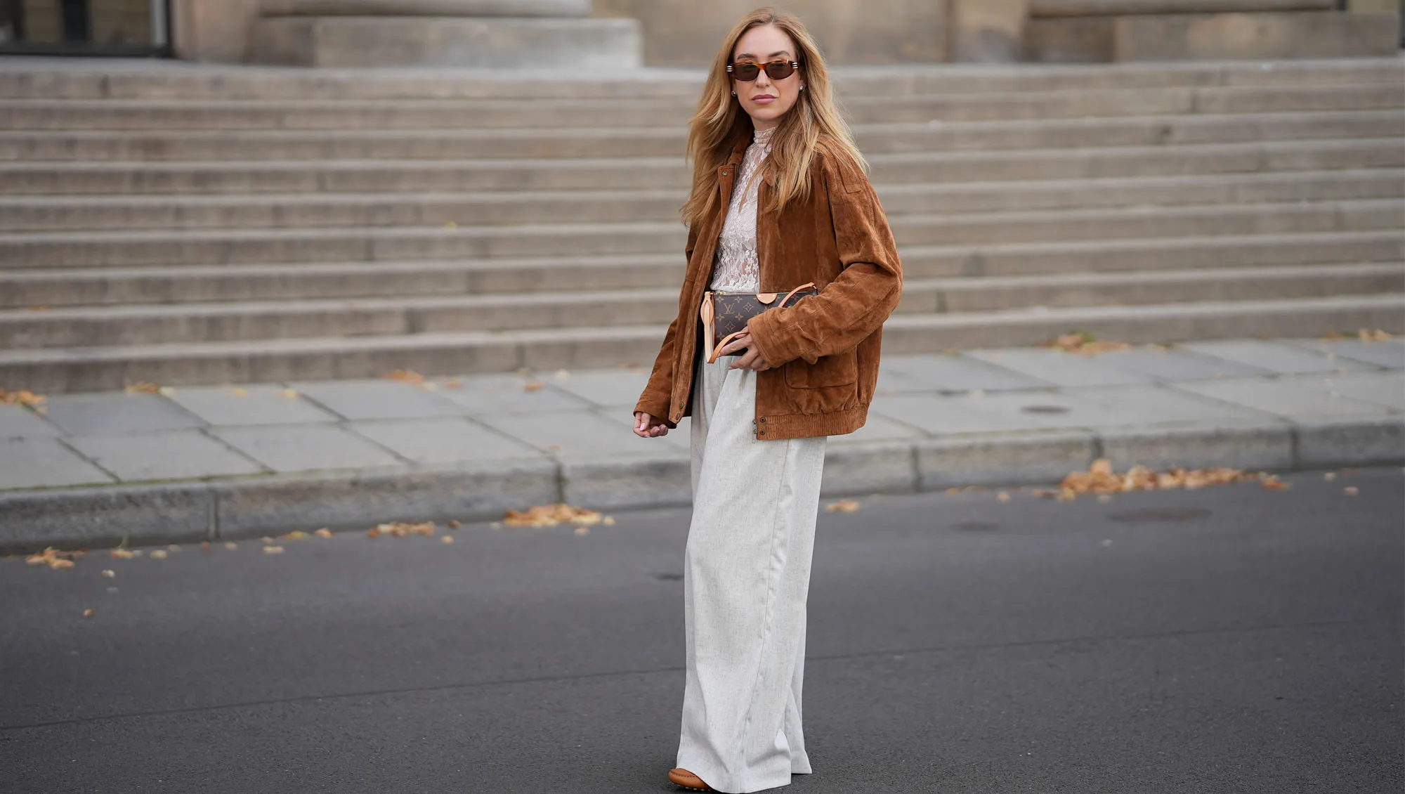 BERLIN, GERMANY - SEPTEMBER 1: Sonia Lyson is seen wearing a white sheer lace high-neck blouse in a soft neutral tone from Baum und Pferdgarten; an oversized brown suede jacket with a relaxed cut and button details from Zara; Wide-leg light beige trousers that drape loosely and reach the floor from Munthe; Cogcnac-colored leather loafers with a classic, structured shape from Tods; a small brown and beige, monogram handbag with tan leather straps and details from Louis Vuitton; rectangular brown sunglasses with a modern shape from Givenchy; her blonde hair ist worn loose with a center part on September 1, 2025 in Berlin, Germany. Reformation Style Deals