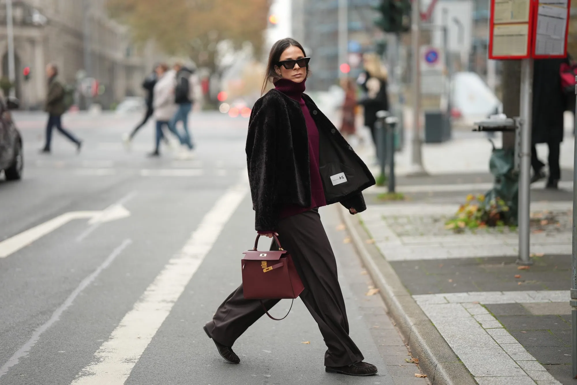 DUESSELDORF, GERMANY - NOVEMBER 10: Patricia Wirschke is seen wearing a dark brown shearling jacket with a boxy cut by Manzoni 24; a burgundy cashmere turtleneck sweater by Van Kukil; wide-leg tailored trousers in dark brown wool by Seductive; brown suede loafers with ruffled stitching by Yves Saint Laurent; a structured burgundy leather “Kelly 25” handbag with gold hardware in Rouge H by Hermès; black cat-eye sunglasses by Phoebe Philo; her brown hair is straight with a center parting and tucked into the collar on November 10, 2025 in Duesseldorf, Germany. (Photo by Moritz Scholz/Getty Images)
