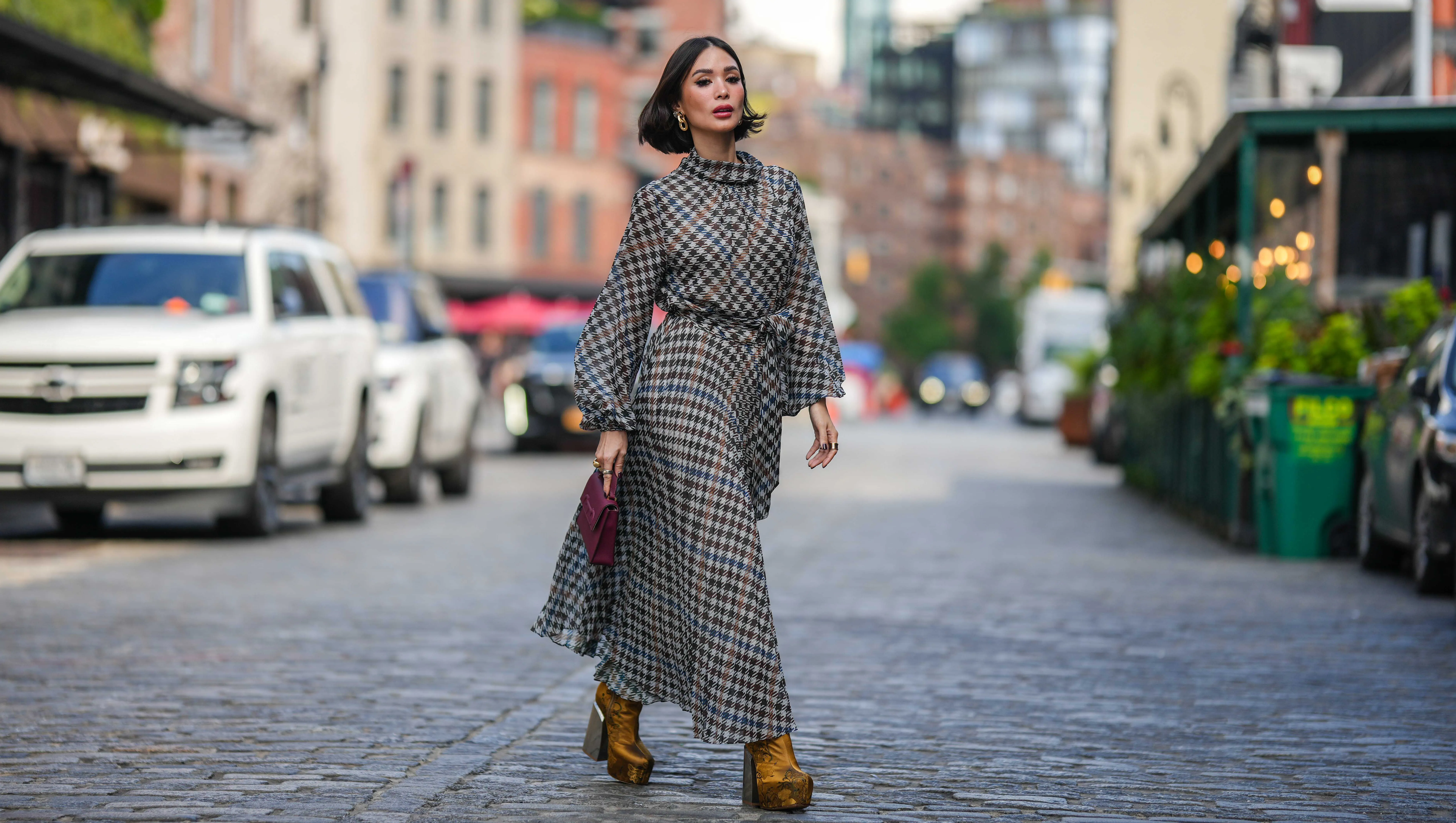 NEW YORK, NEW YORK - SEPTEMBER 12: Heart Evangelista wears golden earrings, a houndstooth pattern printed midi pleated dress, a burgundy leather bag from Carolina Herrera, golden floral print platform boots, outside Carolina Herrera, during New York Fashion Week, on September 12, 2023 in New York City. (Photo by Edward Berthelot/Getty Images)