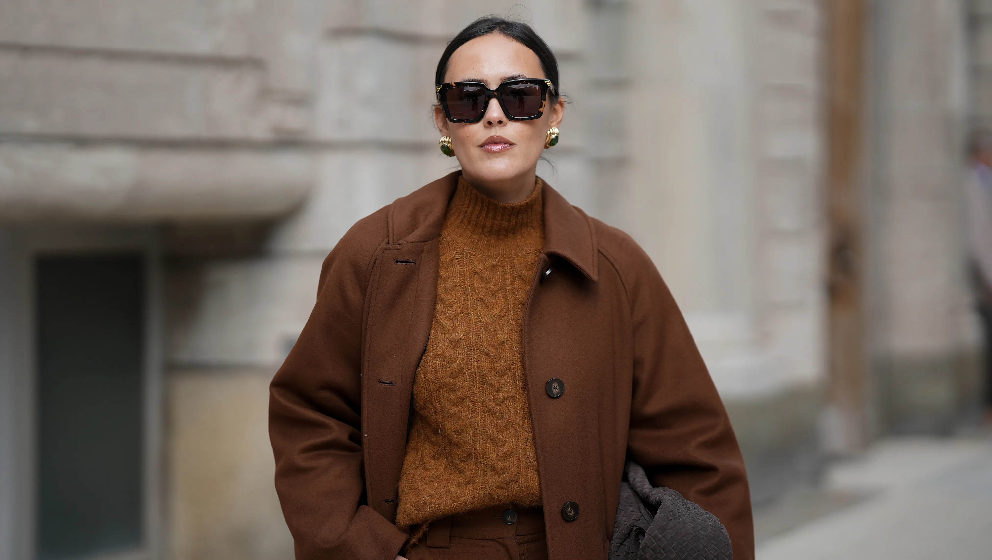 HAMBURG, GERMANY - OCTOBER 16: Laura Noltemeyer is seen wearing a long straight tailored wool coat in chocolate brown with button fastening by S√©zane; high-waisted wide-leg pleated pants by S√©zane; a textured cable knit sweater in a brown tone by S√©zane; a suede asphalt grey shoulder bag with a woven leather structure by Les Visionnaires; square brown sunglasses with gold detailing by Bottega Veneta; gold statement earrings with a green stone detail by Mango; her dark hair is in a low ponytail on October 16, 2025 in Hamburg, Germany. (Photo by Moritz Scholz/Getty Images)