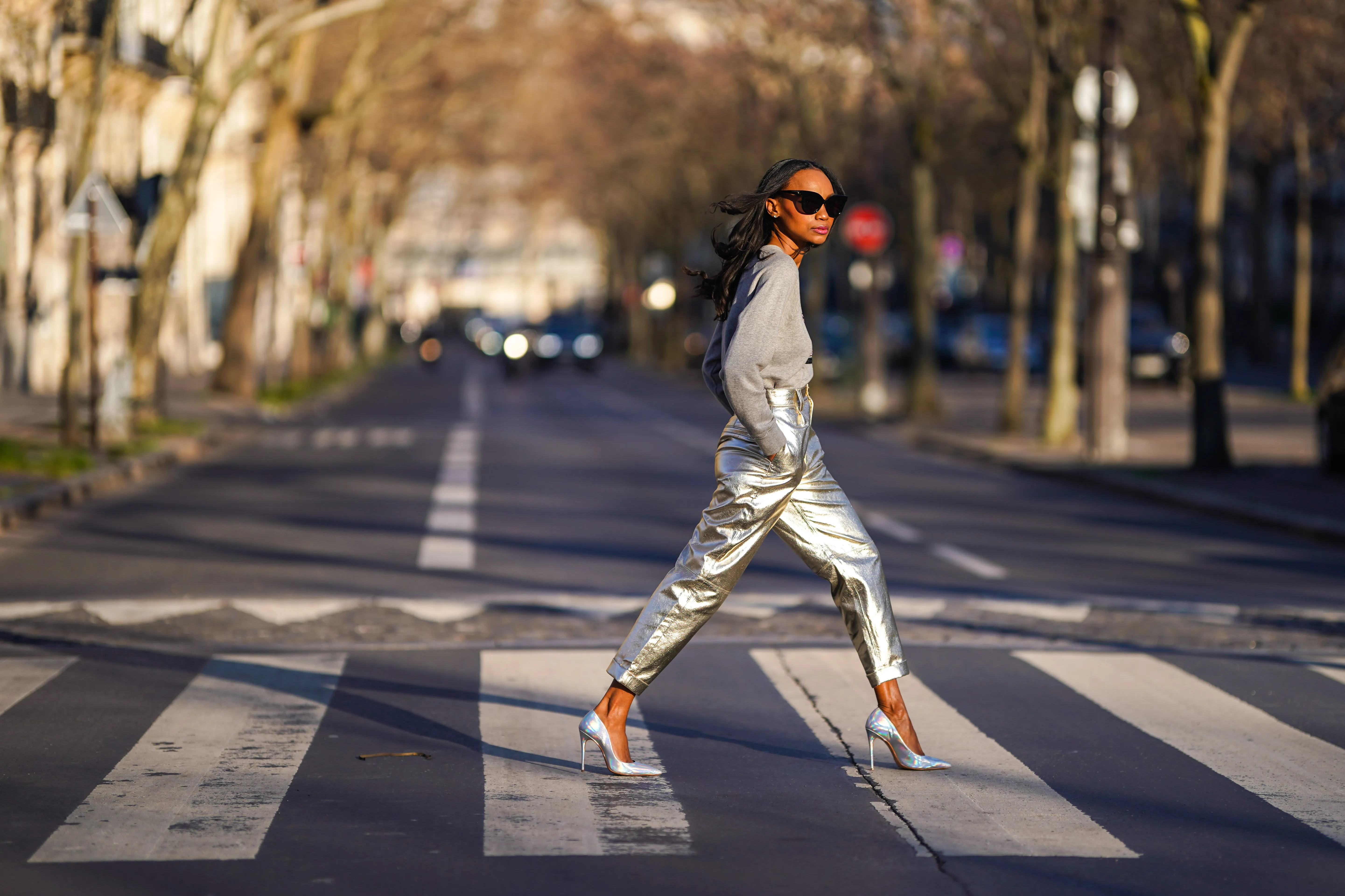 Emilie Joseph @in_fashionwetrust wears sunglasses, a gray logo print sweatshirt with sequins from Marc Jacobs x MTV, high silver and golden shiny pants from Zara, holographic leather silver pointed high heels pumps from Cosmoparis, on February 28, 2021 in Paris, France.