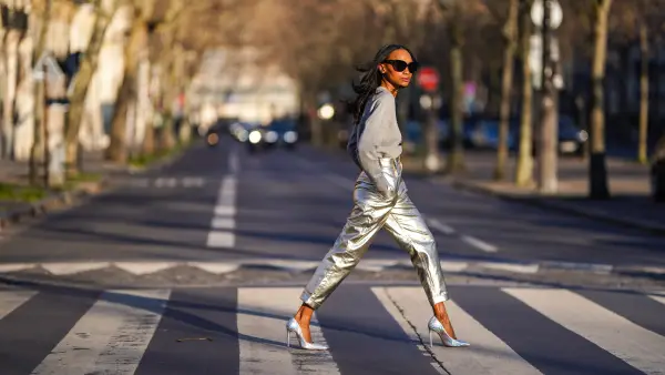 Emilie Joseph @in_fashionwetrust wears sunglasses, a gray logo print sweatshirt with sequins from Marc Jacobs x MTV, high silver and golden shiny pants from Zara, holographic leather silver pointed high heels pumps from Cosmoparis, on February 28, 2021 in Paris, France.