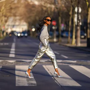 Emilie Joseph @in_fashionwetrust wears sunglasses, a gray logo print sweatshirt with sequins from Marc Jacobs x MTV, high silver and golden shiny pants from Zara, holographic leather silver pointed high heels pumps from Cosmoparis, on February 28, 2021 in Paris, France.