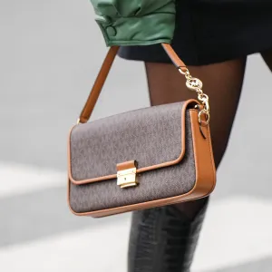 A guest wears a black turtleneck short tube dress, a khaki shiny leather oversized bomber coat, black tights, a brown monogram print pattern in coated canvas handbag from Mickael Kors, black shiny varnished leather crocodile print pattern pointed knees boots, outside Gauchere, during Paris Fashion Week - Womenswear F/W 2022-2023, on March 03, 2022 in Paris, France.