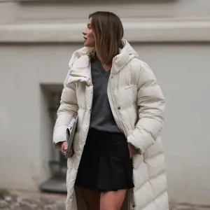 Sophia Geiss is seen wearing a silver nose ring; an outfit from MO&Co. consisting of an ankle-length white quilted jacket, a grey pullover with a ribbed V-neckline underneath, and a black pleated mini skirt; while carrying a MacBook and a newspaper on September 26, 2024 in Berlin, Germany.