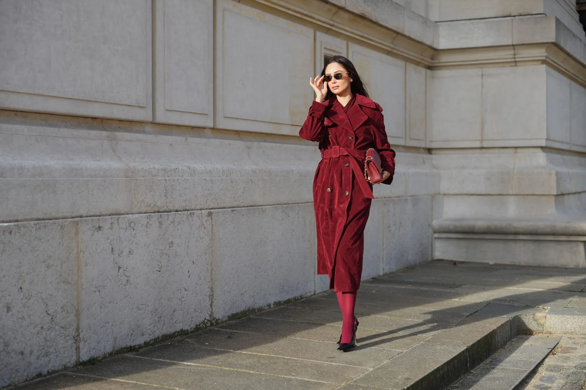 PARIS, FRANCE - DECEMBER 09: Patricia Gloria Contreras wears long straight dark brown hair worn loose, natural skin with neutral lipstick, dark tinted rectangular sunglasses by Bulgari, a burgundy long wool coat worn open by The Frankie Shop with a straight silhouette and wide lapels, burgundy opaque tights, pointed toe high heel pumps by Saint Laurent in black leather, and a burgundy quilted leather shoulder bag with a gold chain strap by Chanel, during a street style fashion photo session, on December 09, 2025 in Paris, France. (Photo by Edward Berthelot/Getty Images)