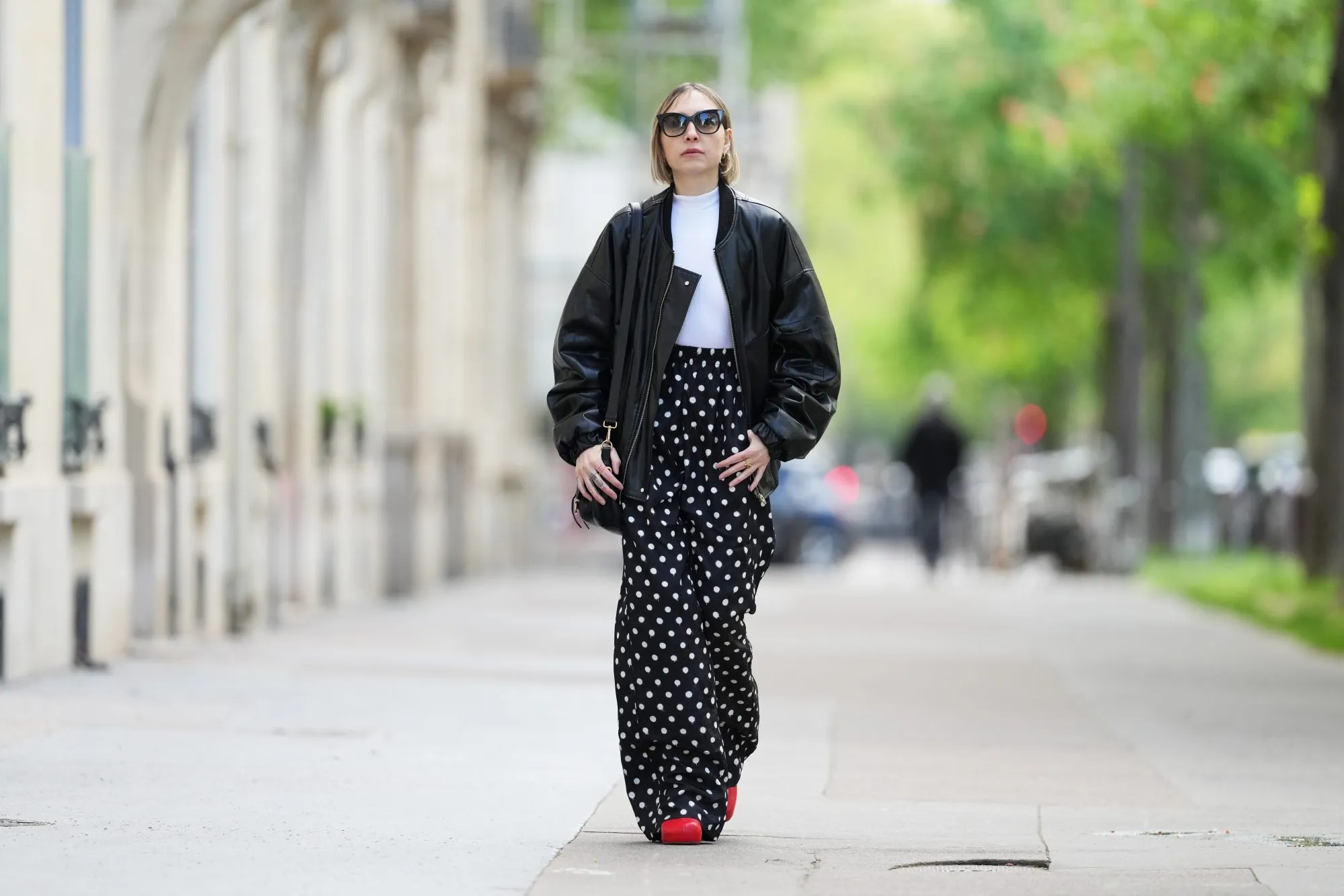 PARIS, FRANCE - APRIL 21: Emy Venturini wears Dite Eyewear Paris sunglasses, a white Intimissimi bodysuit, a black leather bomber jacket, black and white Balenciaga polka dots pants, a black leather Prada bag, golden Chloe rings, red leather Bottega Veneta shoes, during a street style fashion photo session, on April 21, 2024 in Paris, France. (Photo by Edward Berthelot/Getty Images)