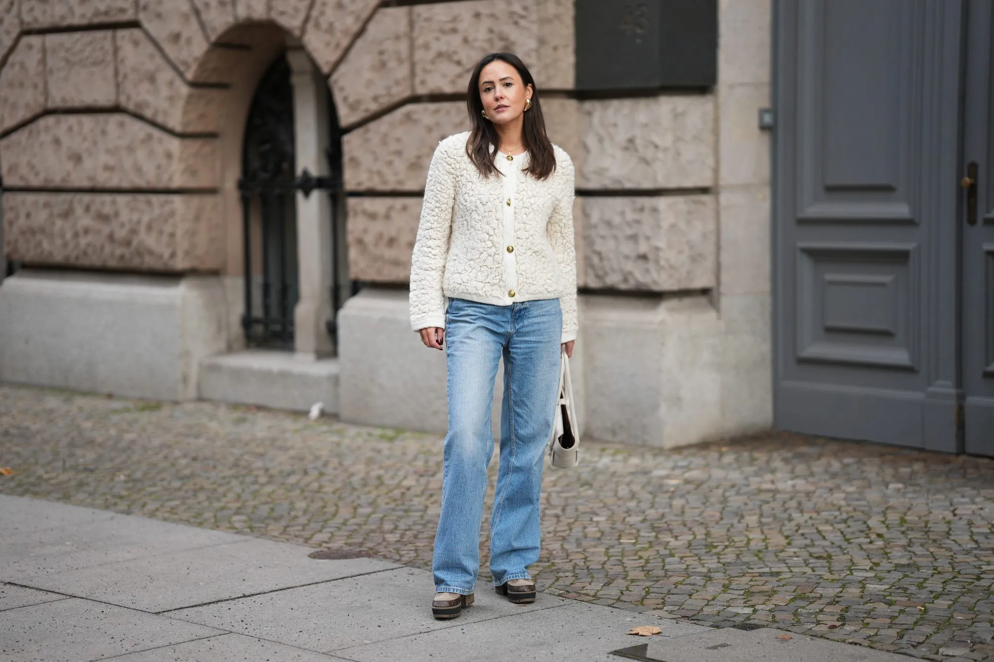 BERLIN, GERMANY - NOVEMBER 25: Laura Noltemeyer is seen wearing a cream textured bouclé knit cardigan with a structured silhouette and gold button fastening from Massimo Dutti; light-blue straight-leg denim trousers with a soft fading in a classic cut from Zara; dark-brown and taupe monogram-detailed leather platform boots with a chunky rubber sole and suede details from Louis Vuitton; a white structured leather top-handle bag in an intrecciato weave and trapeze silhouette called “Intrecciato Tote” from Bottega Veneta; chunky sculptural gold earrings from Zara; her dark brown hair is worn loose, straight and parted in the middle on November 25, 2025 in Berlin, Germany. (Photo by Moritz Scholz/Getty Images)