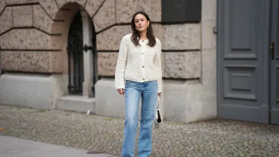 BERLIN, GERMANY - NOVEMBER 25: Laura Noltemeyer is seen wearing a cream textured bouclé knit cardigan with a structured silhouette and gold button fastening from Massimo Dutti; light-blue straight-leg denim trousers with a soft fading in a classic cut from Zara; dark-brown and taupe monogram-detailed leather platform boots with a chunky rubber sole and suede details from Louis Vuitton; a white structured leather top-handle bag in an intrecciato weave and trapeze silhouette called “Intrecciato Tote” from Bottega Veneta; chunky sculptural gold earrings from Zara; her dark brown hair is worn loose, straight and parted in the middle on November 25, 2025 in Berlin, Germany. (Photo by Moritz Scholz/Getty Images)