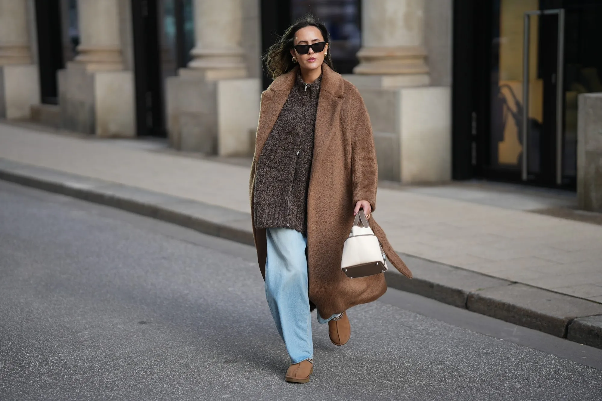 HAMBURG, GERMANY - NOVEMBER 13: Laura Noltemeyer is seen wearing a long camel-colored brushed wool wrap coat with a belt and wide lapels by Max Mara; a chunky zip-front sweater cardigan in a m&eacute;lange brown wool blend with a textured, hand-knit look by by Aylin Koenig; light blue wide-leg jeans in a soft washed denim with a relaxed fit and front tag detail by Closed; chestnut colored suede slippers with plush lining called &bdquo;Tasman&ldquo; by UGG; a structured bucket-shaped handbag in an off-white linen shade with taupe leather handles and lining details called &bdquo;Picotin Cargo 18 Toile Goeland&ldquo; by Herm&egrave;s; black cat eye sunglasses with an acetate frame by Yves Saint Laurent; gold statement earrings with a ruffled surface and a green stone element by Mango ; her brown hair is worn loose in soft waves with a center part on November 13, 2025 in Hamburg, Germany. (Photo by Moritz Scholz/Getty Images)