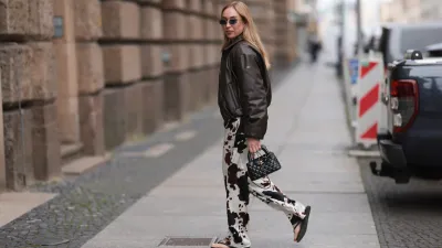 BERLIN, GERMANY - MAY 27: Sonia Lyson is seen wearing round diamond earrings paired with diamond-studded hoop earrings and gold ear studs; rectangular rimless sunglasses with blue lenses and gold temples and bridge from Linda Farrow; a dark brown leather bomber jacket from Alo; a diamond-quilted black leather “Kelly” mini bag from Chanel; wide-leg cow print pants from Zara; and black flip-flops from Havaianas on May 27, 2025 in Berlin, Germany. (Photo by Jeremy Moeller/Getty Images)