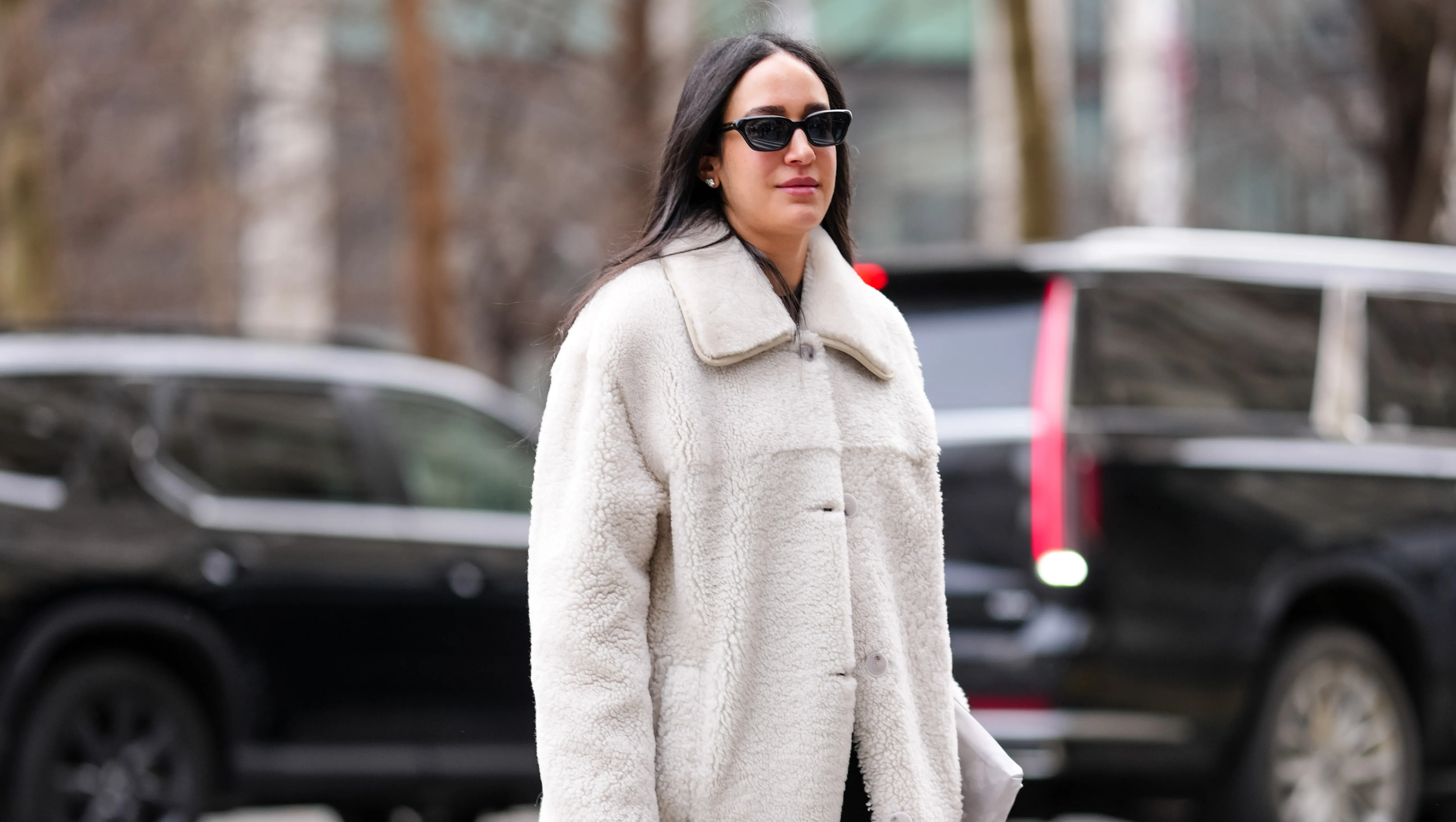 NEW YORK, NEW YORK - FEBRUARY 08: A guest wears black sunglasses, white gold diamond earrings, cream fluffy sherpa coat, shiny black quilted Chanel leather clutch bag, shiny black heeled boots leather shoes, outside Altuzarra, during the New York Fashion week Fall/Winter 2025 on February 8, 2025 in New York, New York. (Photo by Edward Berthelot/Getty Images)