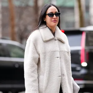 NEW YORK, NEW YORK - FEBRUARY 08: A guest wears black sunglasses, white gold diamond earrings, cream fluffy sherpa coat, shiny black quilted Chanel leather clutch bag, shiny black heeled boots leather shoes, outside Altuzarra, during the New York Fashion week Fall/Winter 2025 on February 8, 2025 in New York, New York. (Photo by Edward Berthelot/Getty Images)