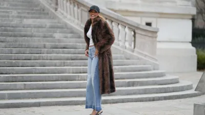 PARIS, FRANCE - DECEMBER 11: Alicia Aylies wears hair pulled back into a sleek low ponytail, natural skin with defined brows and lipstick, a black baseball NY cap, a white fitted cropped top by Celine, a long brown faux fur coat with a straight cut and button closure, light blue high waist flared wide leg jeans with a raw hem, and dark pointed toe high heel pumps shoes, during a street style fashion photo session, on December 11, 2025 in Paris, France. (Photo by Edward Berthelot/Getty Images)