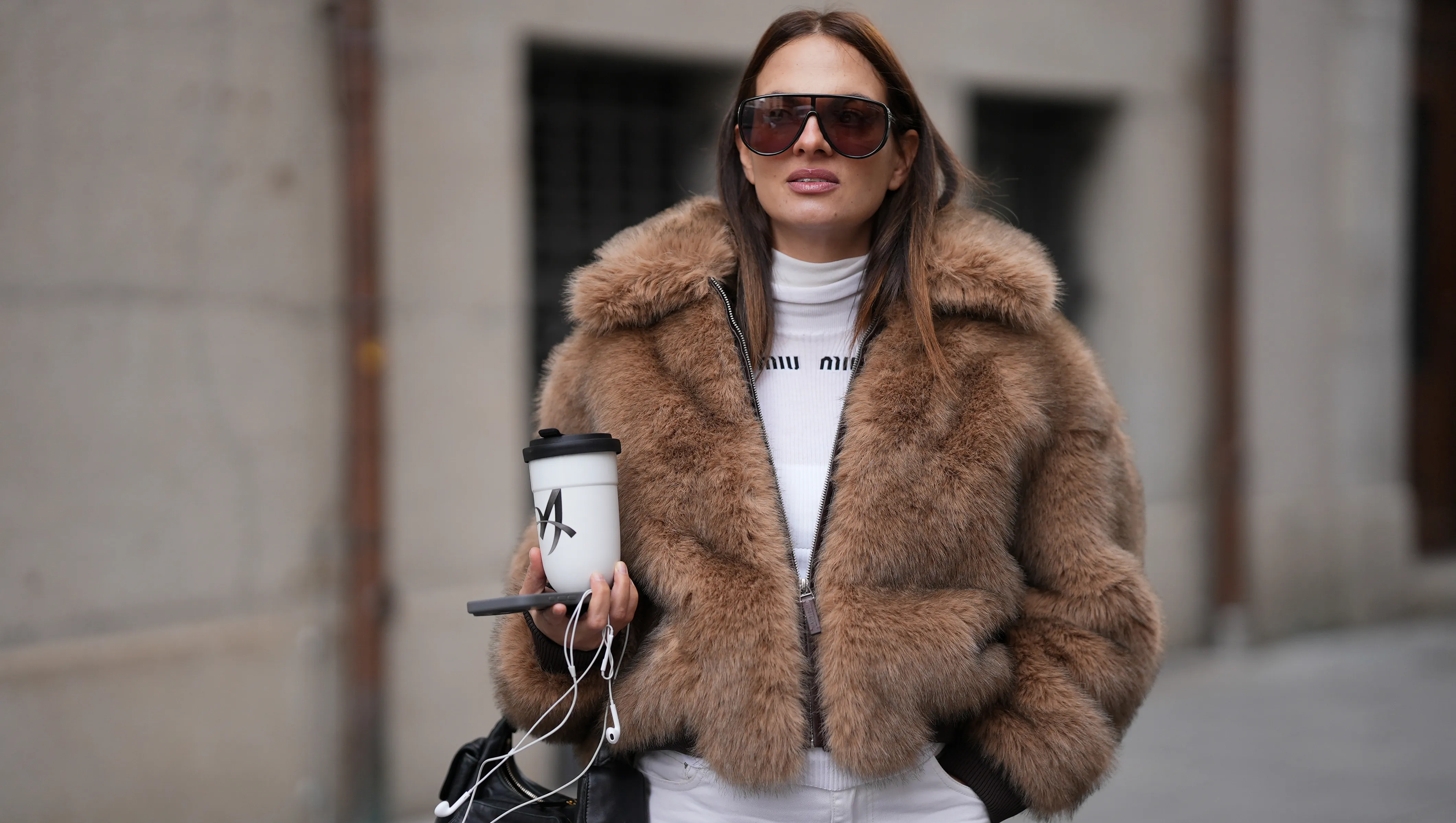 MUNICH, GERMANY - NOVEMBER 19: Anna Winter is seen wearing a cropped faux-fur jacket in a warm hazelnut brown tone with a dense, plush texture, voluminous collar and front zip from Worst Behaviour; a fitted white ribbed shirt with a high crew neckline and front logo stitching from Miu Miu; wide-leg white denim trousers with a relaxed drape from The Frankie Shop; a black leather handbag with multiple pocket detailing and gold hardware called ‚ÄûNappa Leather Pocket Bag‚Äú from Miu Miu; oversized aviator sunglasses with a softly curved top line and brown tinted lenses from Tom Ford; she is carrying a white porcelain to-go cup from KPM; her brunette hair is styled straight with a middle part on November 19, 2025 in Munich, Germany. (Photo by Moritz Scholz/Getty Images)