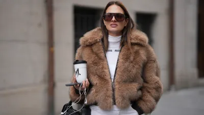 MUNICH, GERMANY - NOVEMBER 19: Anna Winter is seen wearing a cropped faux-fur jacket in a warm hazelnut brown tone with a dense, plush texture, voluminous collar and front zip from Worst Behaviour; a fitted white ribbed shirt with a high crew neckline and front logo stitching from Miu Miu; wide-leg white denim trousers with a relaxed drape from The Frankie Shop; a black leather handbag with multiple pocket detailing and gold hardware called „Nappa Leather Pocket Bag“ from Miu Miu; oversized aviator sunglasses with a softly curved top line and brown tinted lenses from Tom Ford; she is carrying a white porcelain to-go cup from KPM; her brunette hair is styled straight with a middle part on November 19, 2025 in Munich, Germany. (Photo by Moritz Scholz/Getty Images)