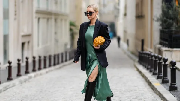 PARIS, FRANCE - JANUARY 25: Justyna Czernia wears sunglasses, gold earrings, a green mint satin silk slit / split long dress, a black oversized blazer jacket, an orange shiny leather puffy handbag from Bottega Veneta, black shiny leather pointed high boots, gold ring, outside Alexis Mabille, during Paris Fashion Week - Haute Couture Spring/Summer 2022, on January 25, 2022 in Paris, France. (Photo by Edward Berthelot/Getty Images)
