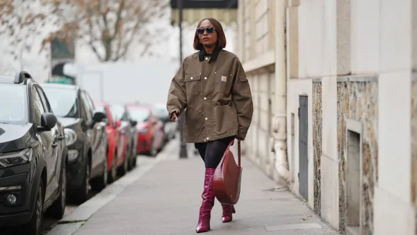 PARIS, FRANCE - DECEMBER 13: Carrole Sagba wears a straight chin-length bob hairstyle with a center part, makeup featuring a natural complexion with soft pink lipstick, an olive green khaki cotton canvas workwear jacket with flap chest pockets and snap-button fastening by Carhartt, black opaque tights, a burgundy leather tote bag with a structured silhouette and crocodile pattern, and burgundy shiny knee-high leather boots with a pointed toe and block heel and crocodile pattern, during a street style fashion photo session, on December 13, 2025 in Paris, France. (Photo by Edward Berthelot/Getty Images)