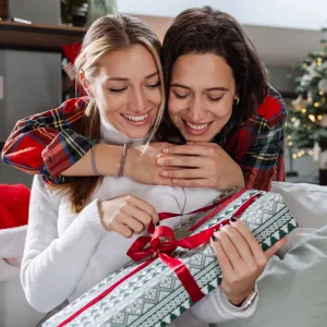 Two young woman embracing at home and exchanging gifts