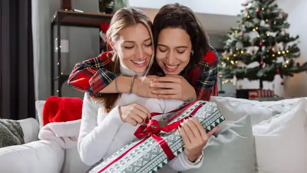 Two young woman embracing at home and exchanging gifts