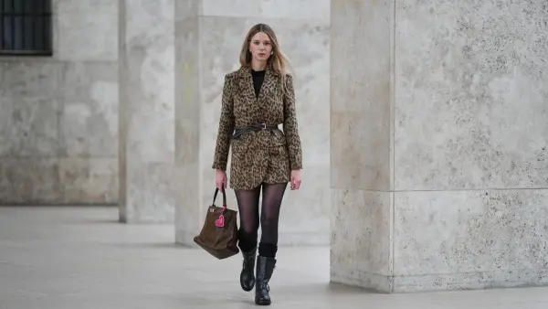 PARIS, FRANCE - DECEMBER 13: Natalia Verza wears long straight blonde hair with a center part, makeup featuring a natural complexion with pale pink lipstick, an animal cheetah print tailored jacket by Zadig & Voltaire with structured shoulders, cinched at the waist with a black leather belt by Miu Miu, sheer black tights, black leather biker boots by Jimmy Choo Re Edition 2008 with a mid-calf height and buckle details, and a brown leather shoulder bag by Zadig & Voltaire with a soft slouchy shape, a neon pikn heart-shaped charm,, during a street style fashion photo session, on December 13, 2025 in Paris, France. (Photo by Edward Berthelot/Getty Images)