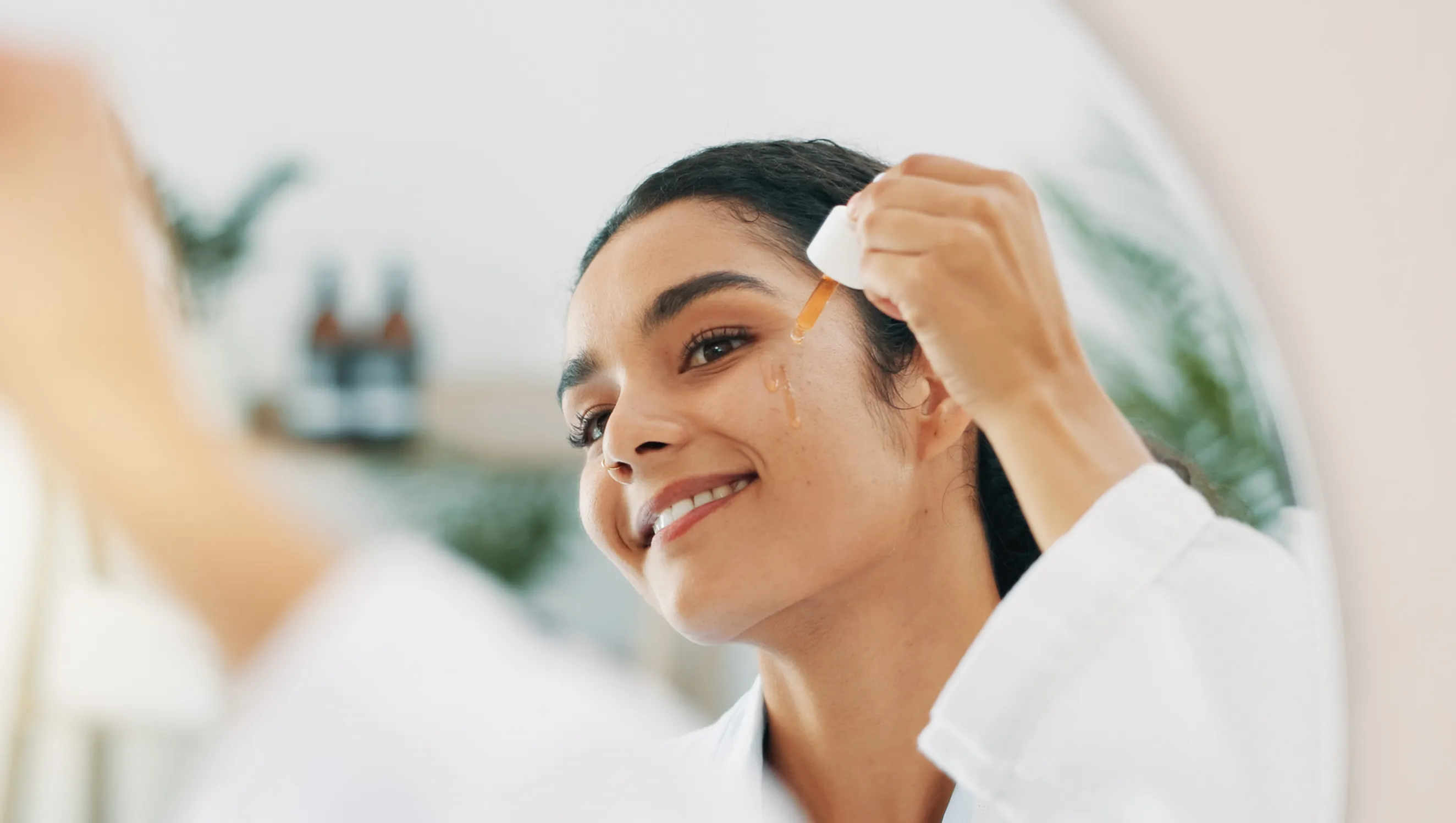 Happy woman, mirror or serum with dropper for facial cleanse, anti aging treatment or oil in bathroom at home. Face, female person and moisturizer with smile for skincare, pamper or collagen at house