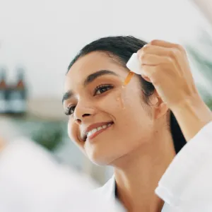 Happy woman, mirror or serum with dropper for facial cleanse, anti aging treatment or oil in bathroom at home. Face, female person and moisturizer with smile for skincare, pamper or collagen at house